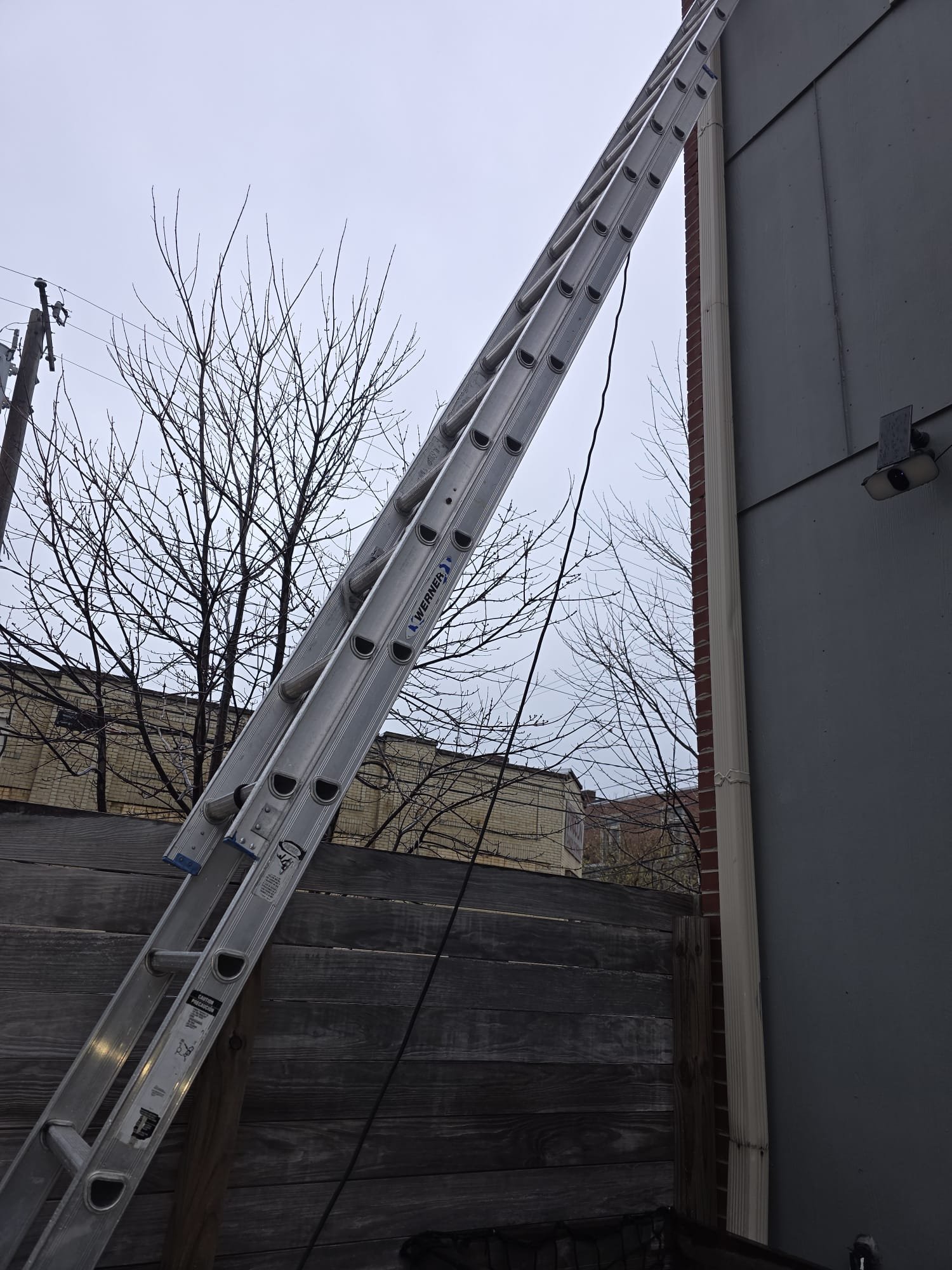 Extension ladder set against a condominium building for dryer vent access