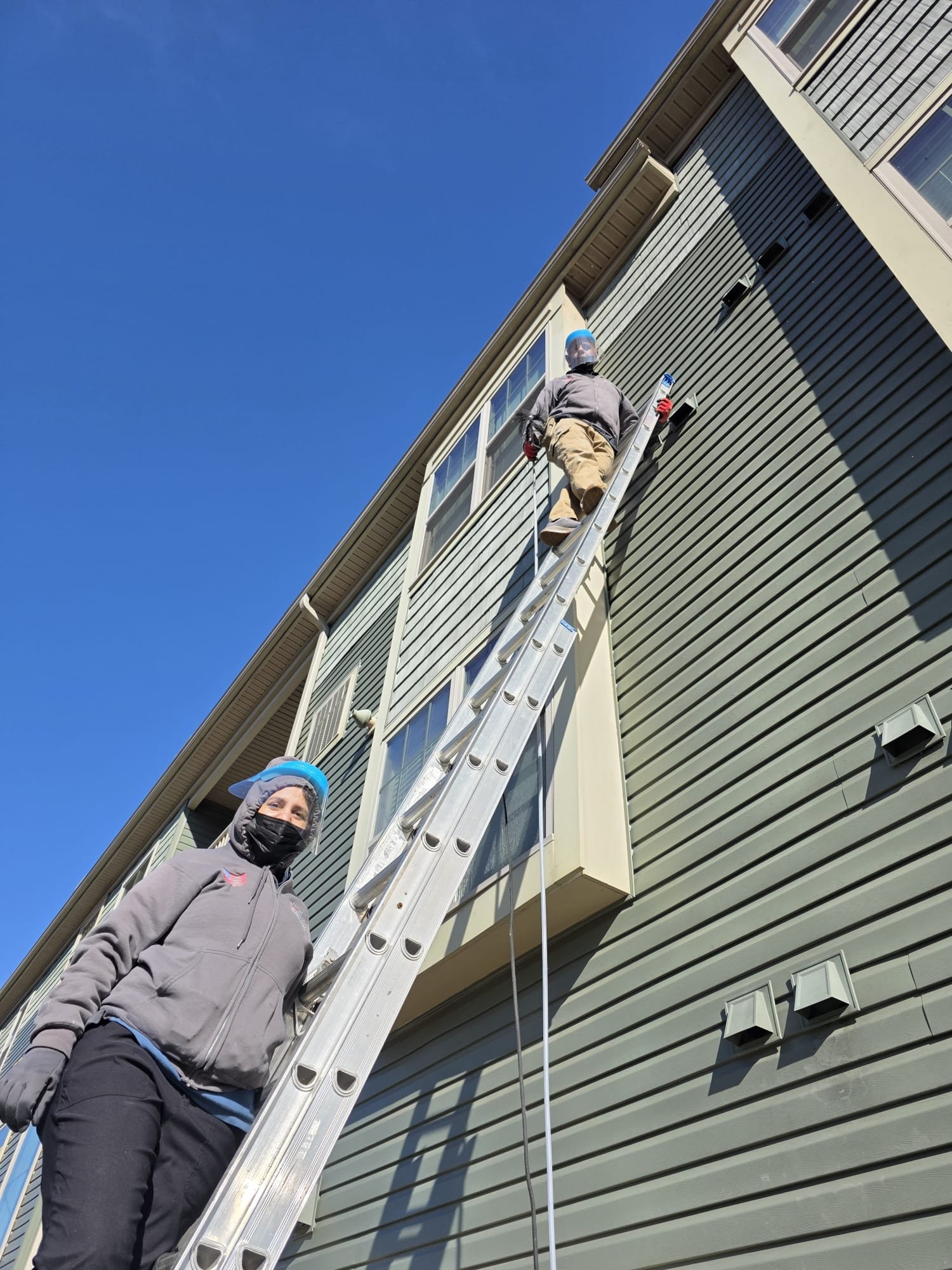 Technician on a tall ladder servicing a condominium building's dryer vents
