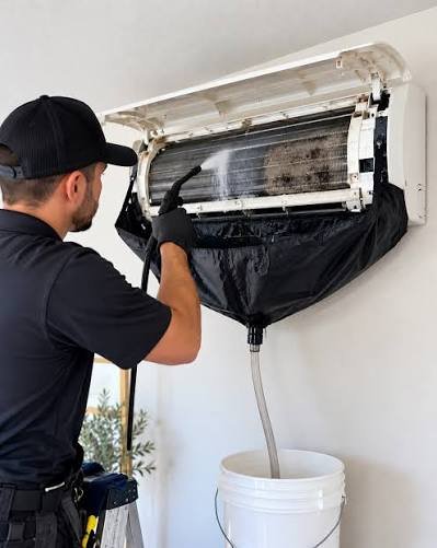 Technician pressure-washing a mini-split with wash bag