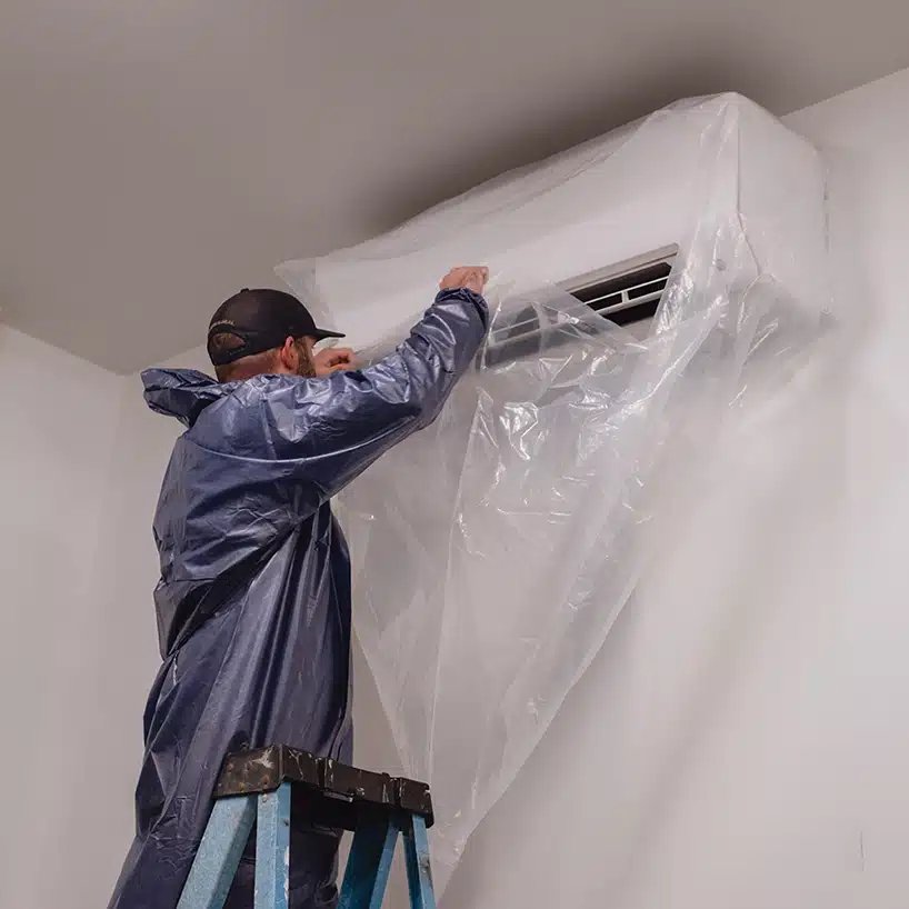 Technician wrapping a mini-split in protective sheeting